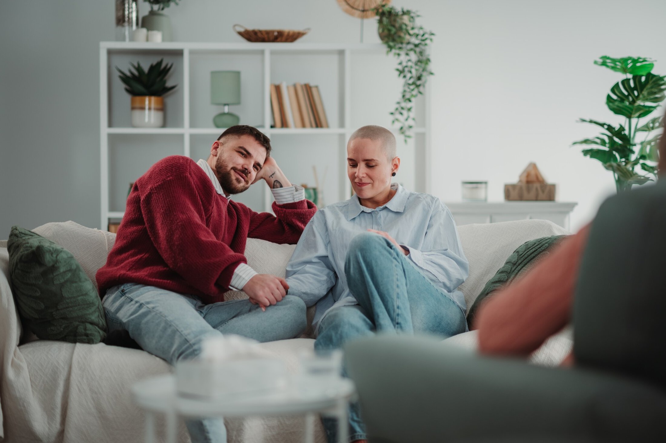 Couple sitting on a couch in a living room, holding hands and receiving support during a counseling session