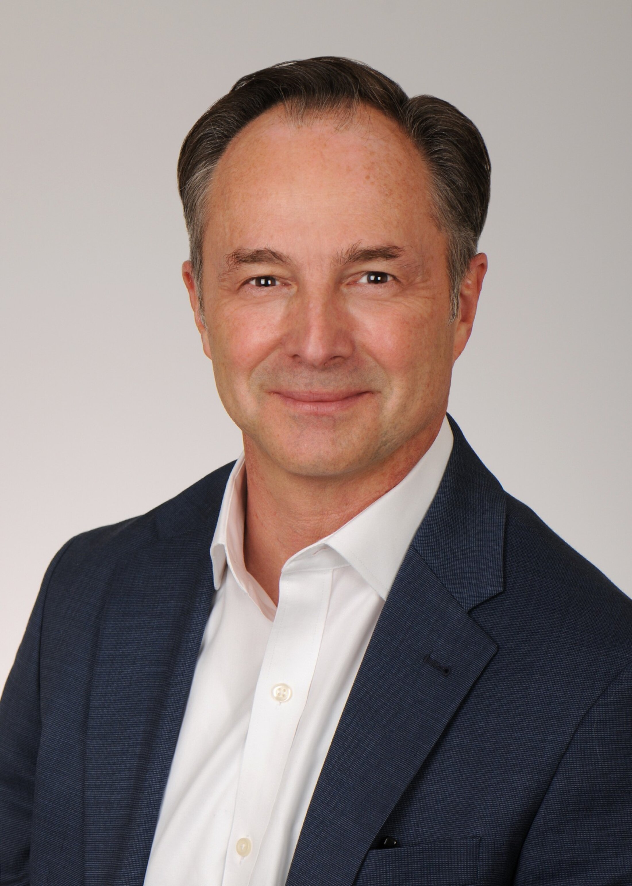 Headshot of man who is smiling. He is wearing an open-collared white shirt and blue jacket.