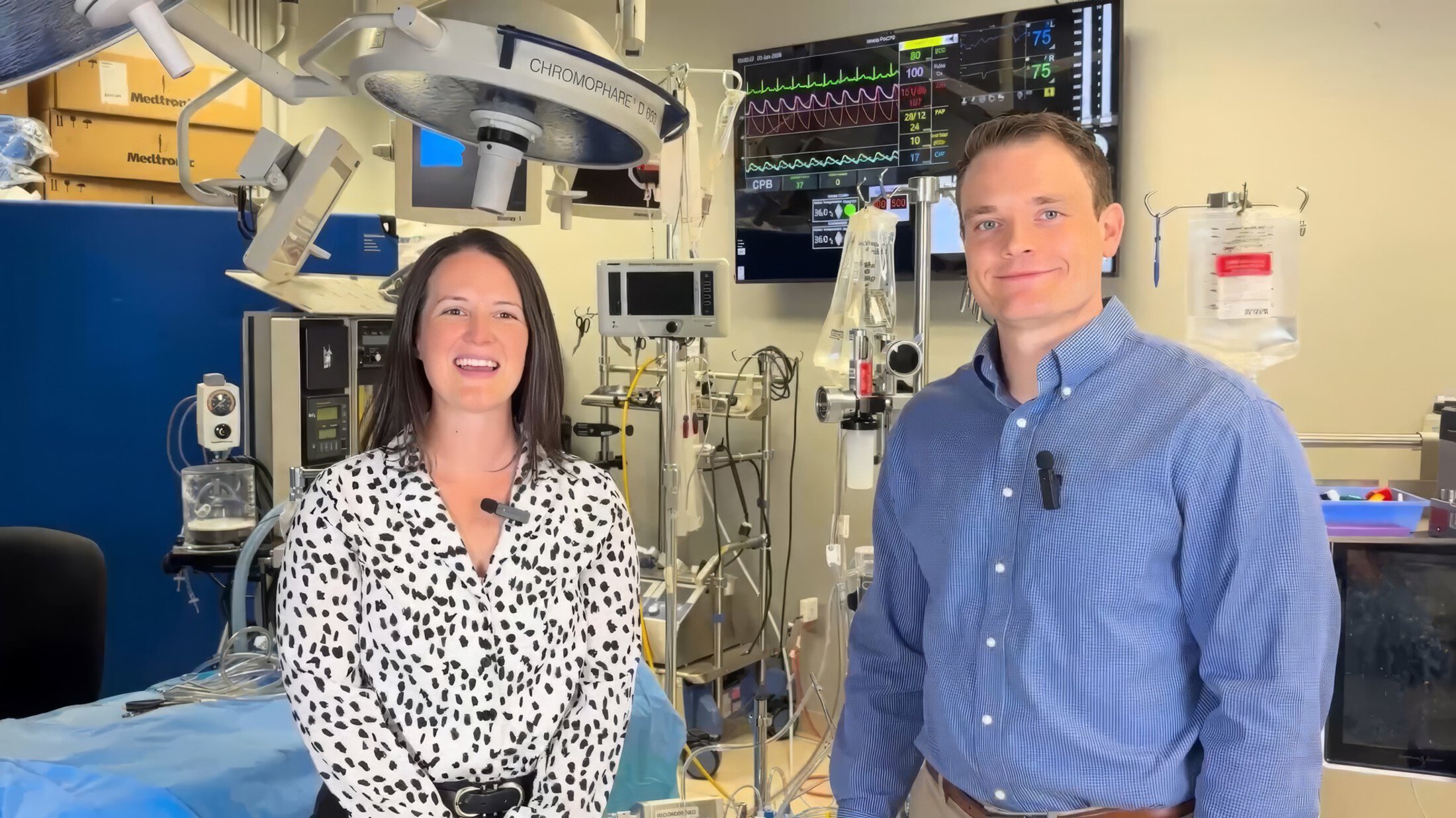 A woman and man in professional attire speak to the camera while standing in a perfusion simulation lab.