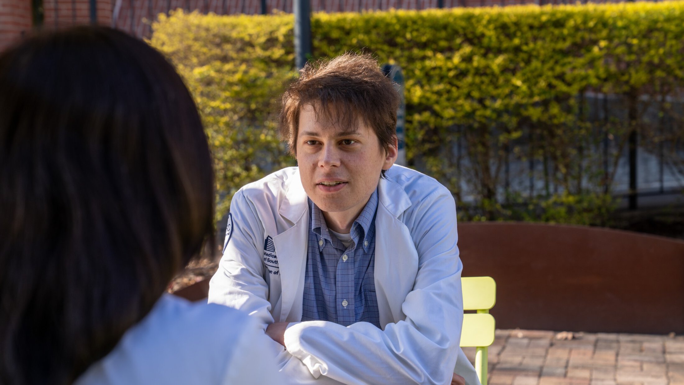 A medical student leans forward intently as he listens to another student.
