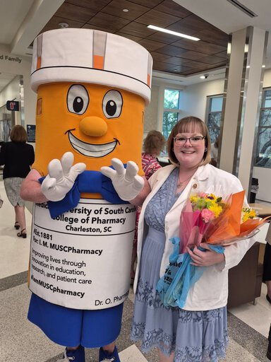 Woman holding a bouquet stands with a person dressed as a giant pill bottle.
