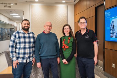 Four people standing together in a modern medical university lobby, smiling for a group photo, with a digital MUSC display visible in the background.