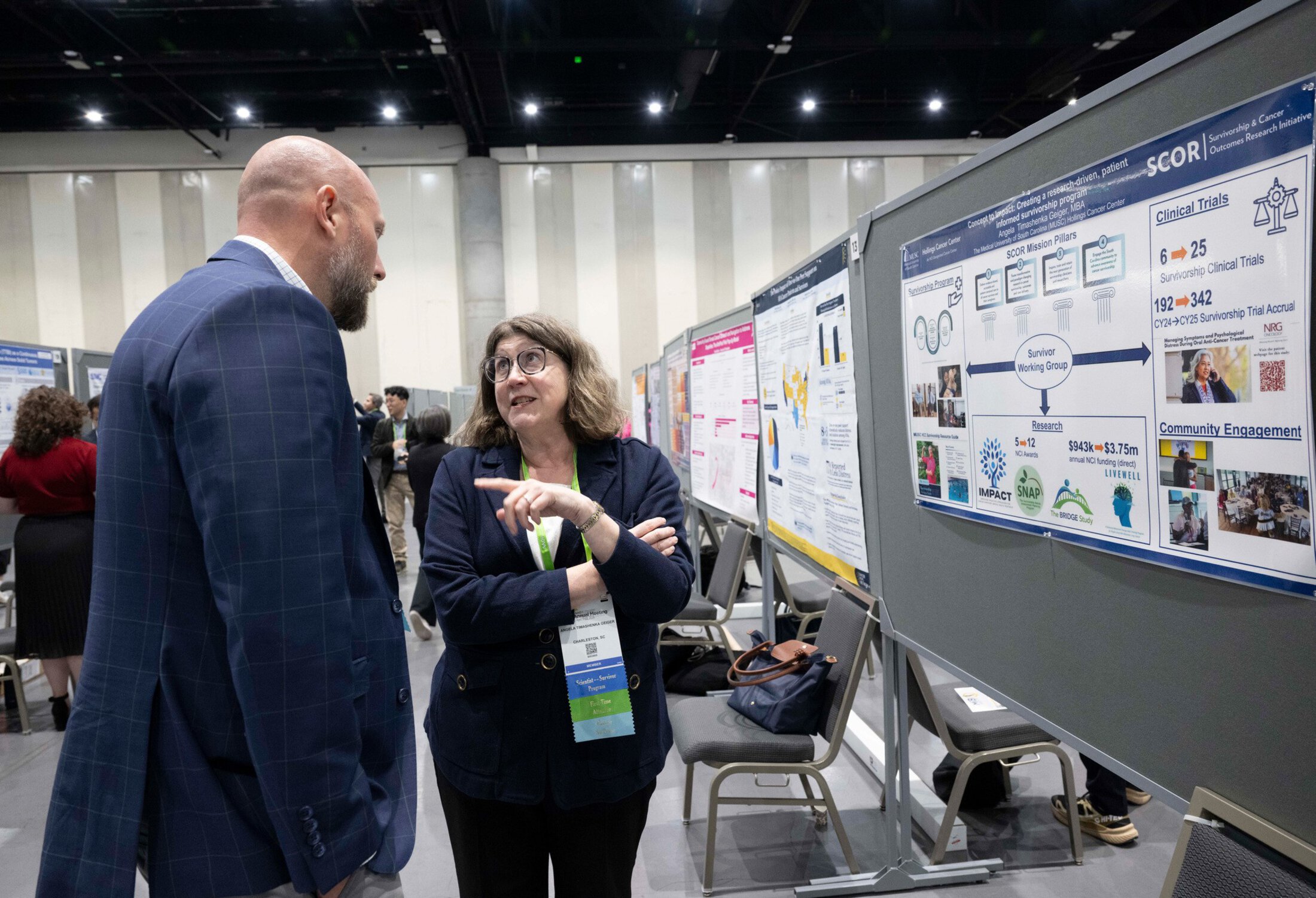 A woman talks with a man in front of her poster at a conference.