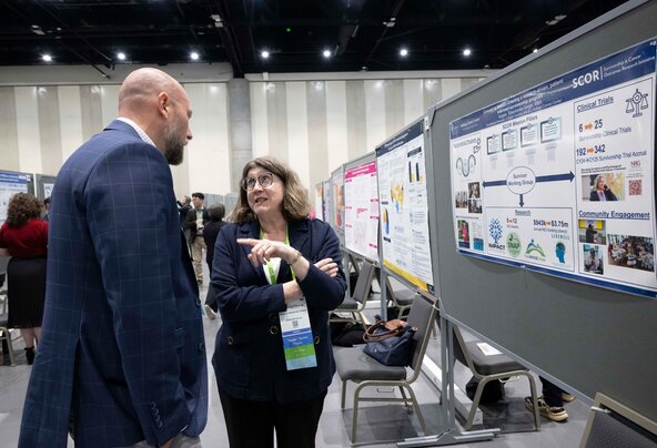 A woman talks with a man in front of her poster at a conference.