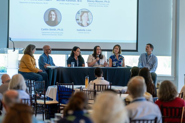 Six people seated at a table on a stage participate in a panel discussion.