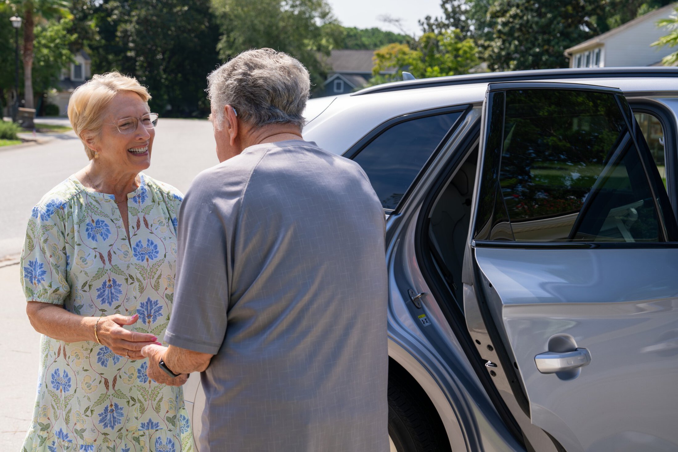 A woman smiles and greets an older man as he prepares to get into the back seat of a car.