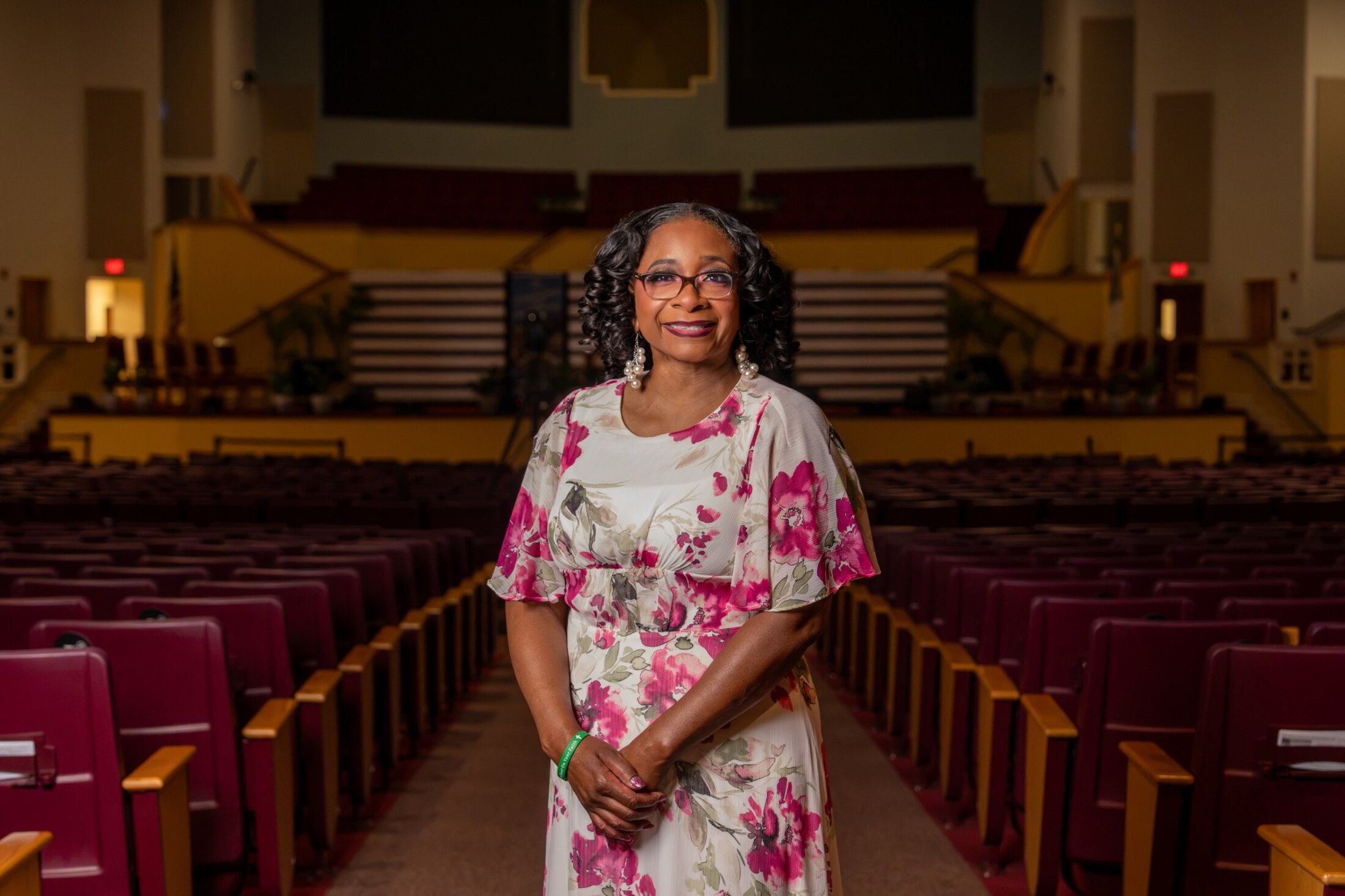 Michelle Brown Nelson, wearing a pink floral dress, poses for a portrait in the empty and darkened sanctuary at Mount Moriah Missionary Baptist Church.