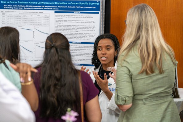 A student speaks to a small group in front of a poster about her research.