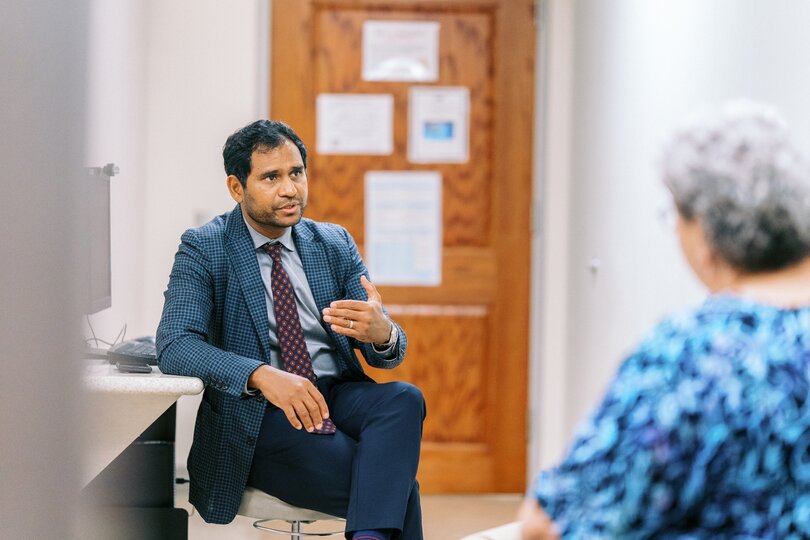 A doctor sits and talks to a woman in an exam room.