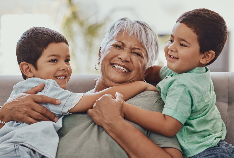 An older woman smiles joyfully as two young boys hug her.