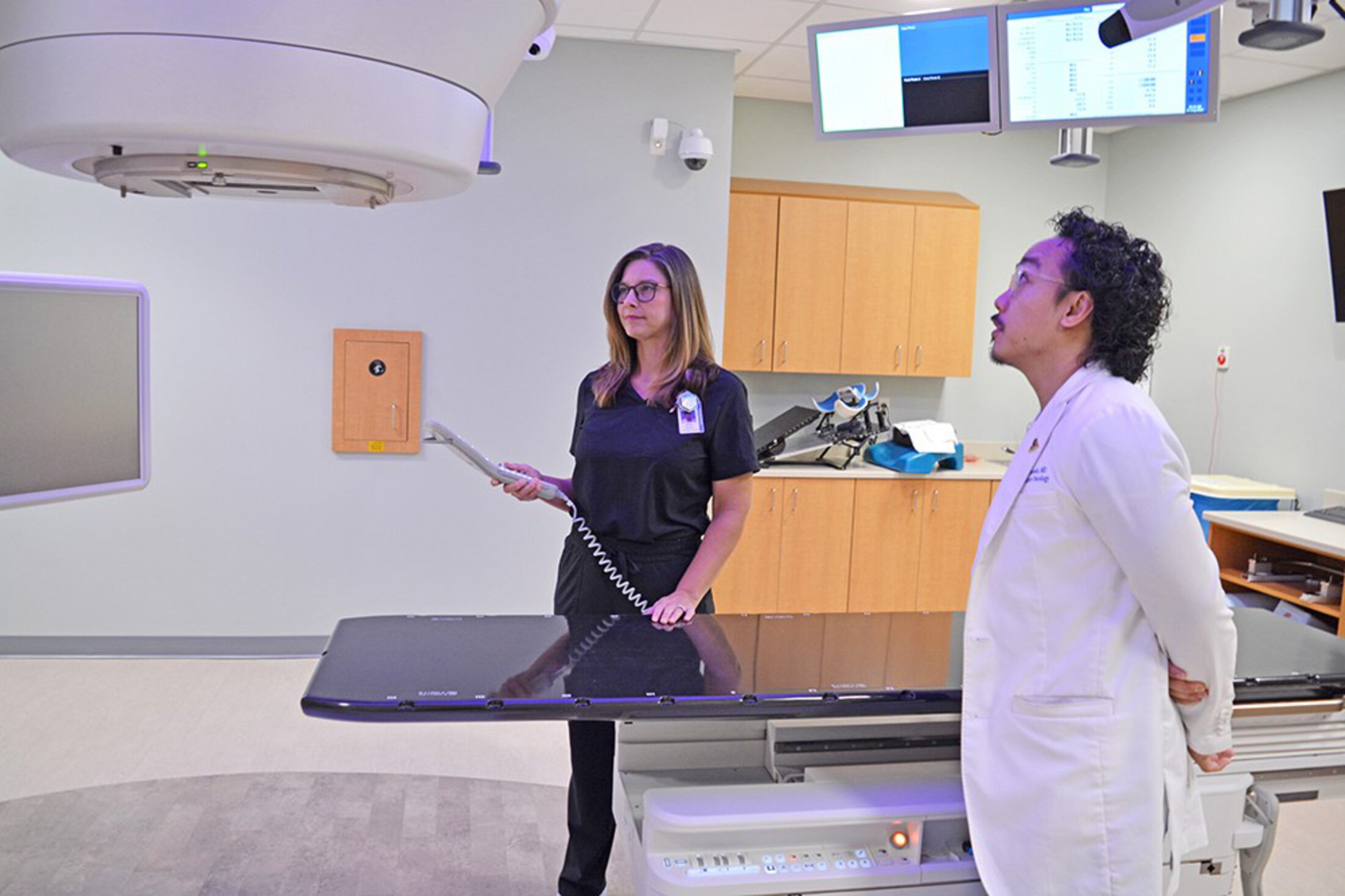A physician and a tech look up at a radiation therapy machine.