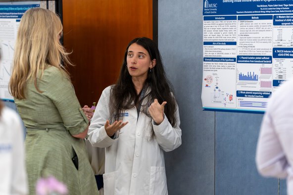 A student speaks to someone in front of a poster about her research.