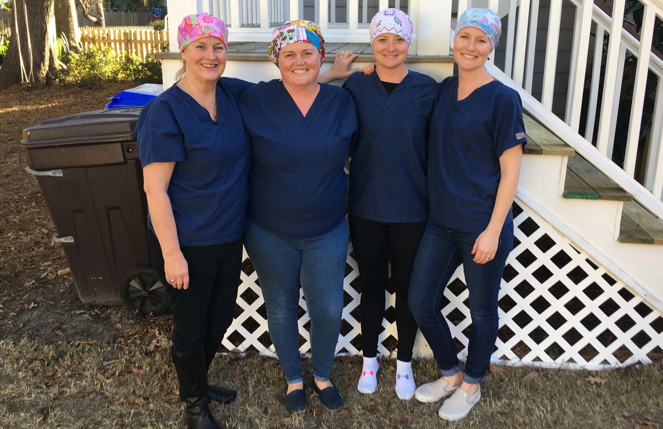 Four women standing outside. All are wearing blue scrubs and head coverings.