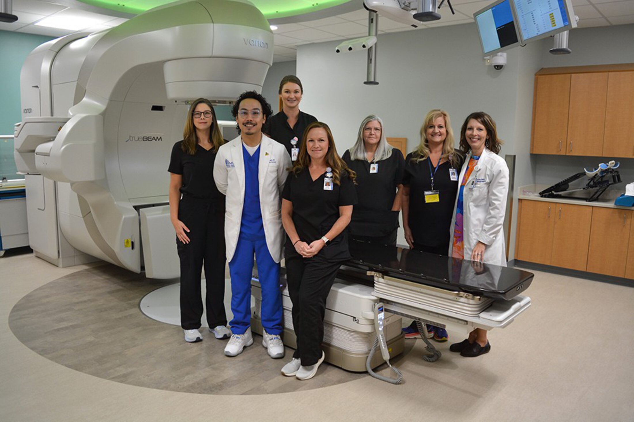 The radiation oncology team poses next to a linear accelerator.