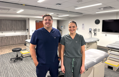 a man and a woman wearing scrubs pose in a student learning lab for physician assistants