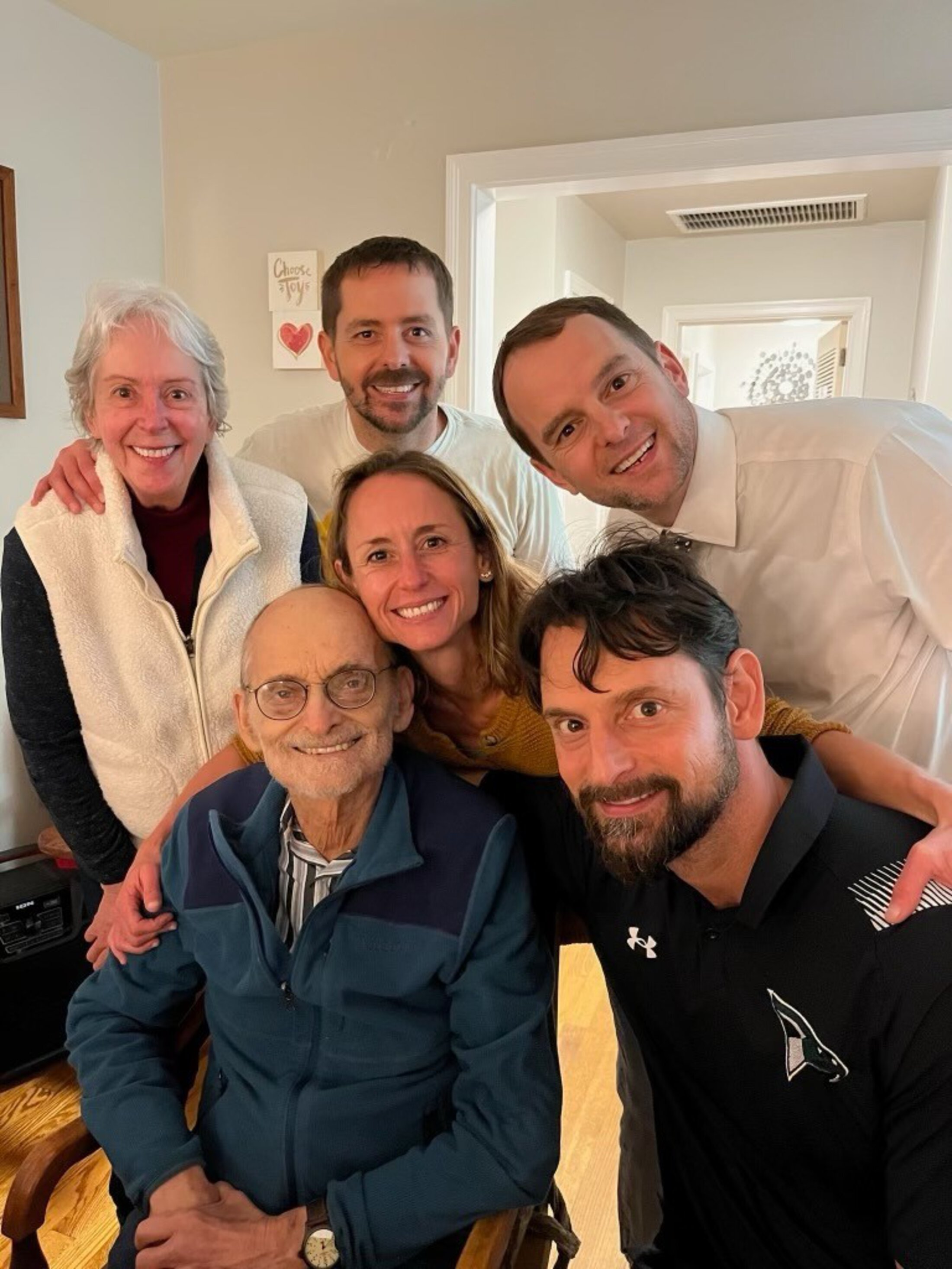 Four adult children crowd around their mom and dad for a selfie.