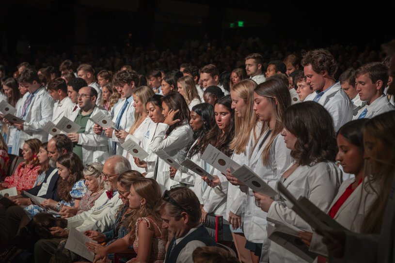 MUSC College of Medicine white coat audience reading booklet in auditorium