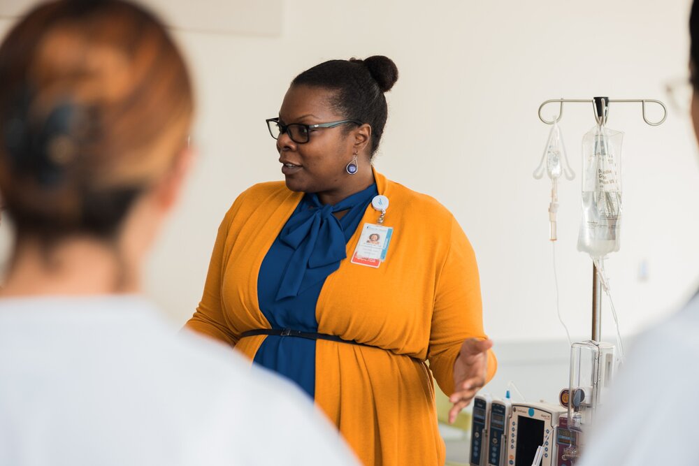 a woman instructs students will standing beside an IV drip