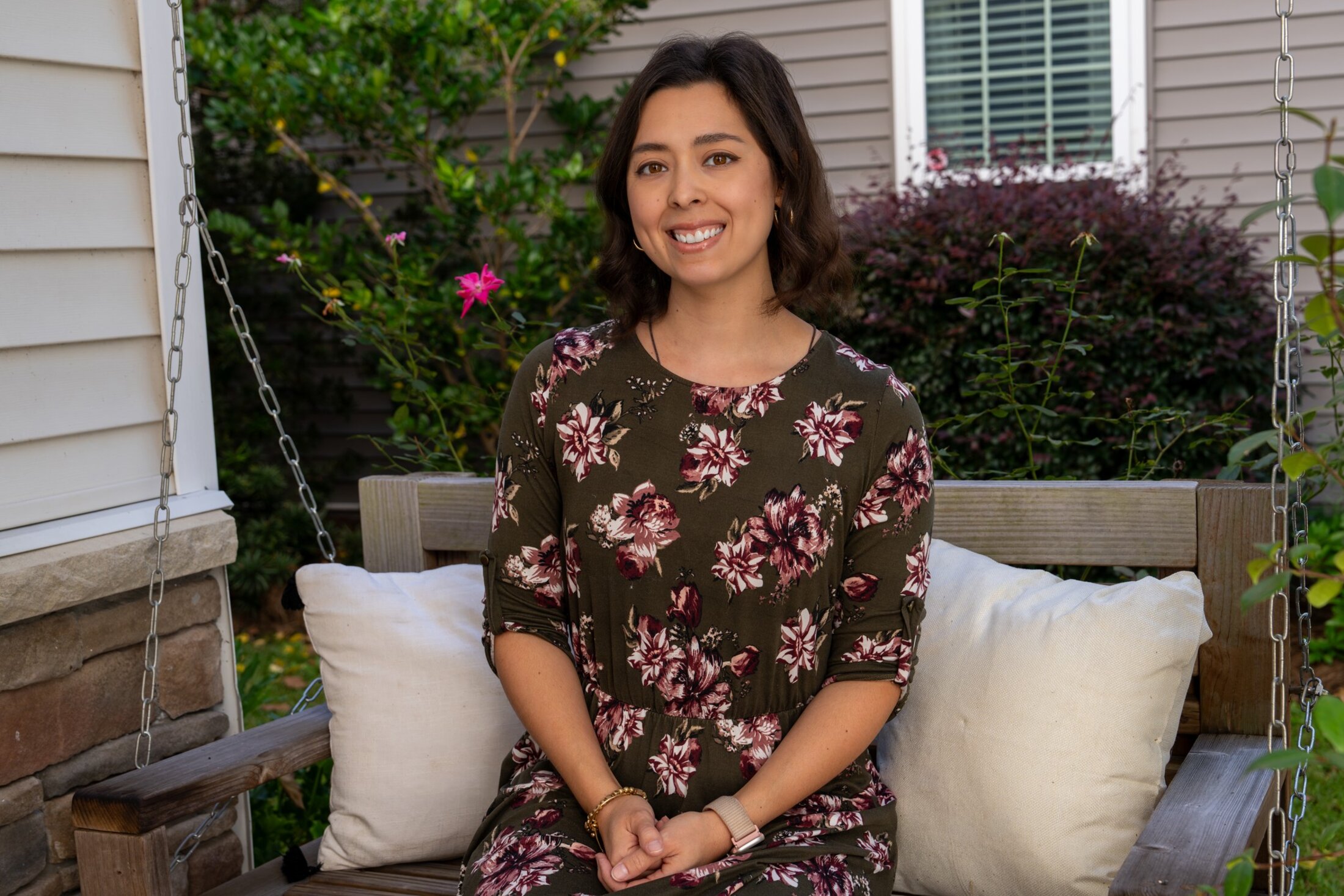 Devin Barnett sits on a hanging swing on her porch, surrounded by plants and flowers.