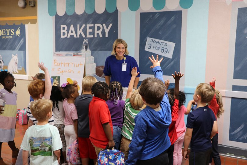 Woman giving a nutrition lesson to a group of children with their hands raised.
