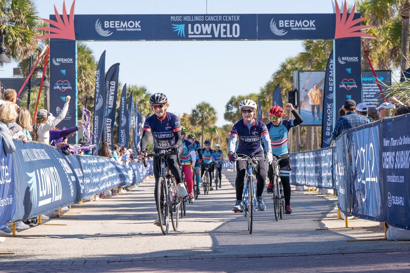 a group of riders pass under the finish line truss at Lowvelo25 with people on either side cheering them on