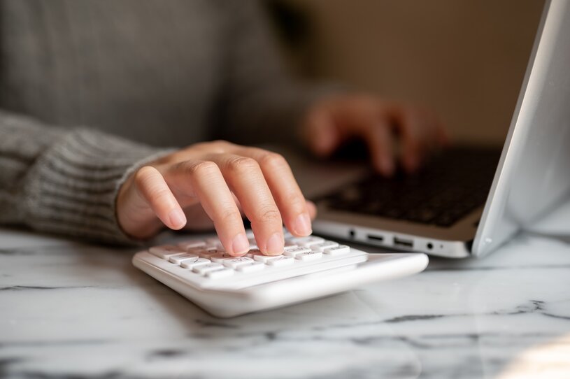 A cropped shot of a woman working at a table indoors, typing on a laptop keyboard, and using a calculator. multitasking skill, busy businesswoman, accounting