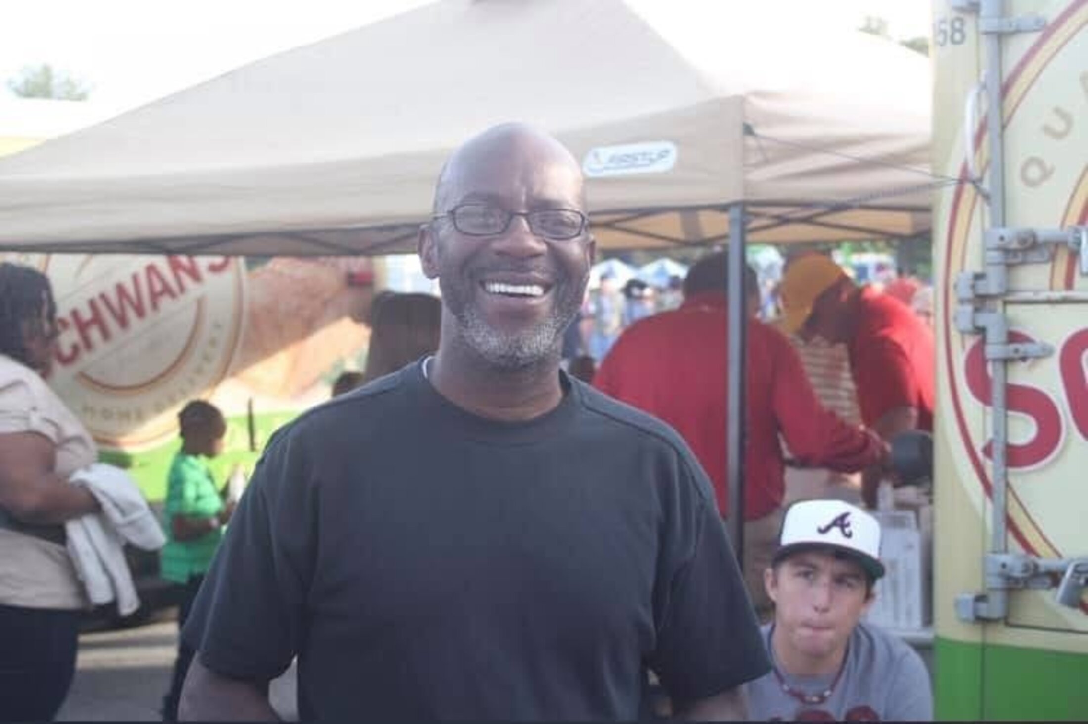 A man smiles broadly while at an outdoor festival.