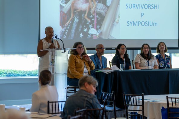 A woman speaks at a podium with members of a panel seated at a table next to her.