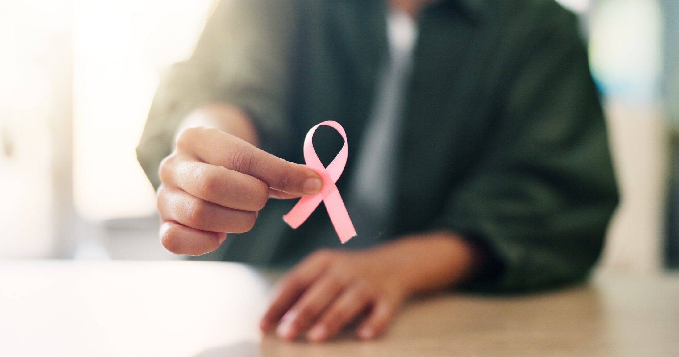 A woman holds a pink ribbon.