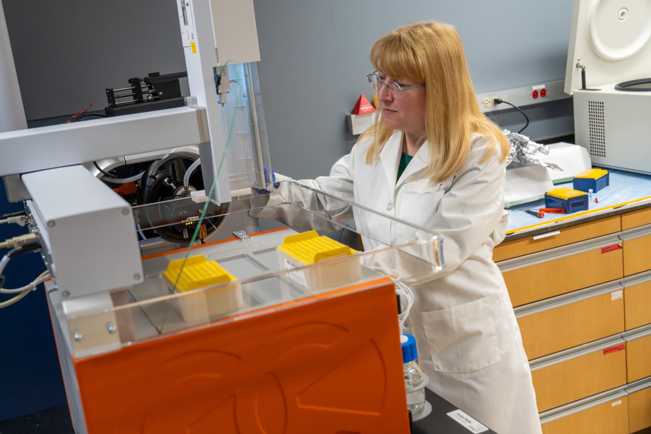 A researcher in a white lab coat works with a complicated machine in a lab.