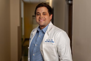 Adam Fox in a white doctor's coat in a clinic hallway