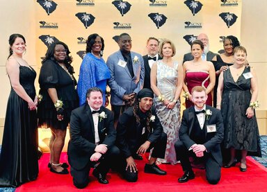 A group of nurses stand together at a gala in formal attire.