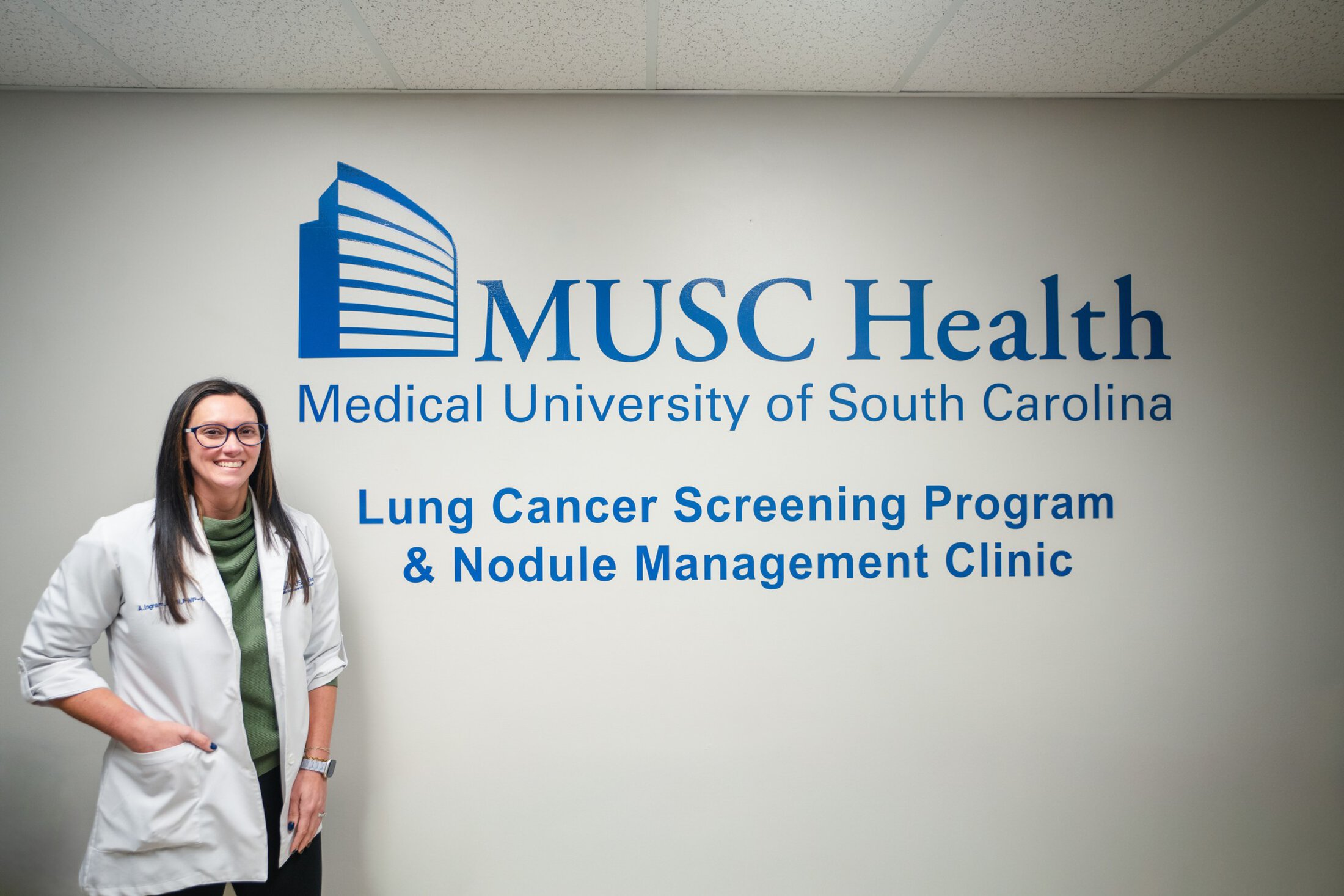 Alex Ingram, FNP-C, wearing a white coat standing in front of the MUSC Health Lung Cancer Screening Program and Nodule Management Clinic signage