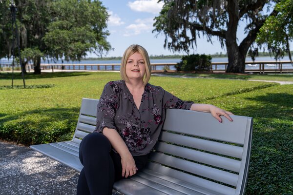 A woman relaxes on a bench in a riverside park.