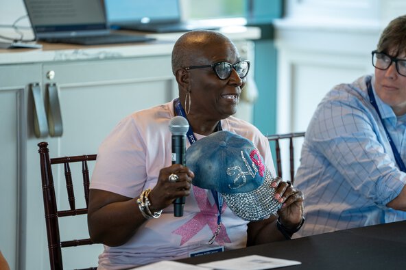 While speaking as part of a panel discussion, a cancer survivor holds up a hat with sequins that spell Hope with a cancer ribbon in place of the p.