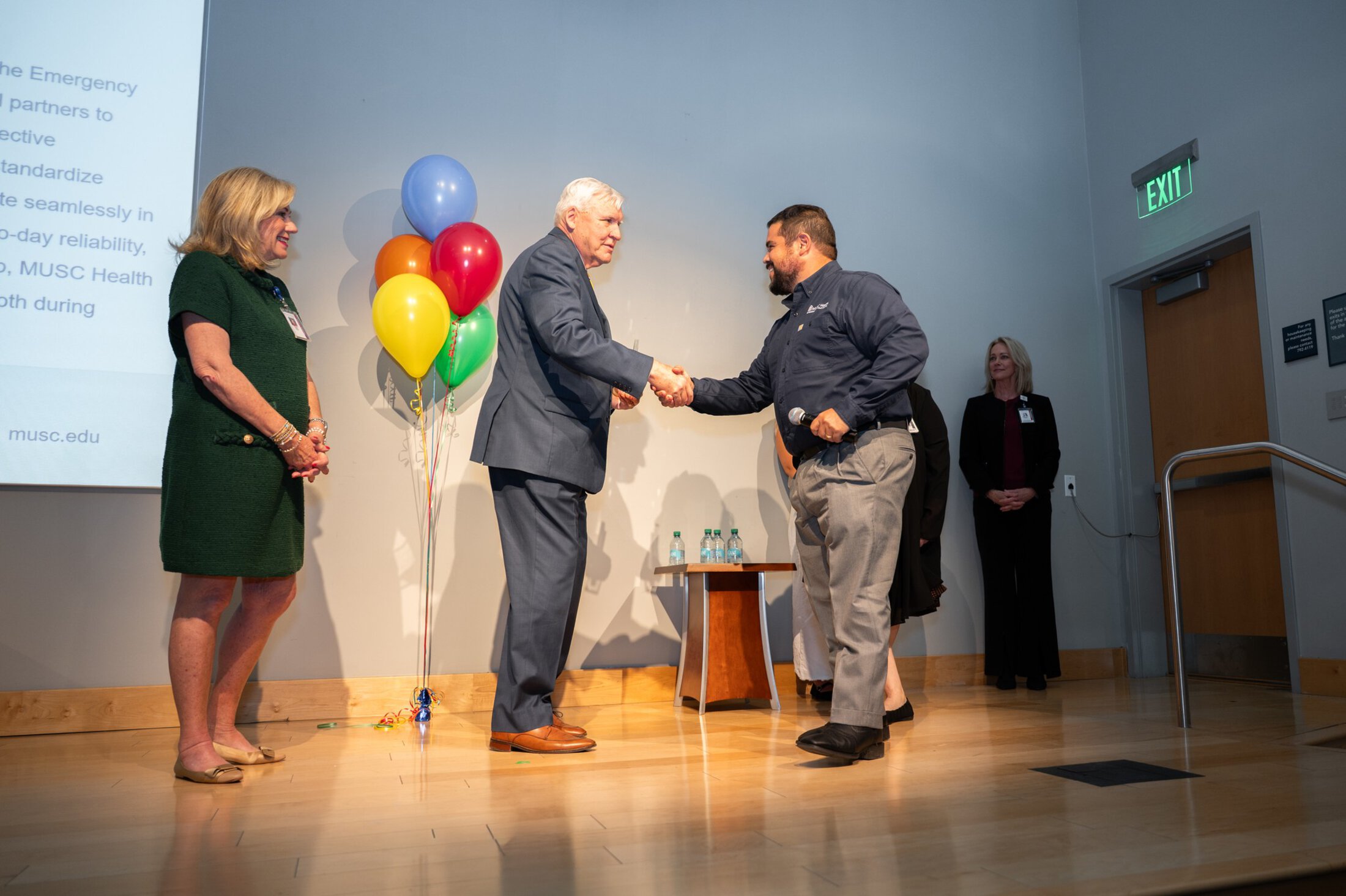 VIA Driggers shakes Dr Coles hand, Dr Cole and Mrs Cole standing on a stage