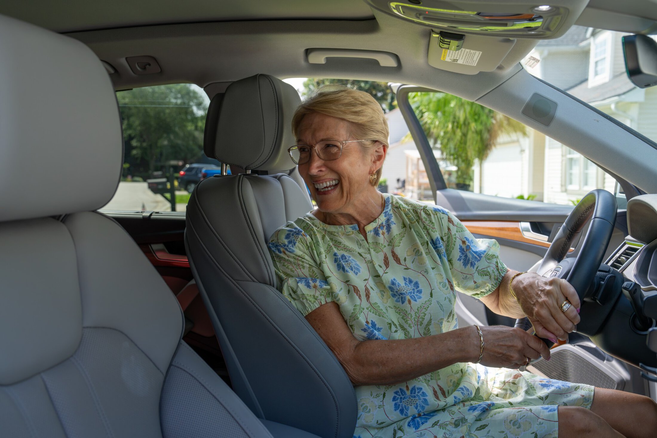 A woman in the driver's seat of a car twists around to look into the back seat and smiles.