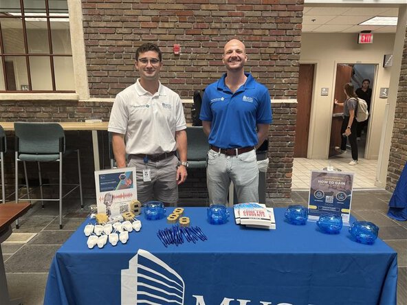 Two staff members stand behind a MUSC table with financial literacy materials and giveaways at an indoor tabling event.