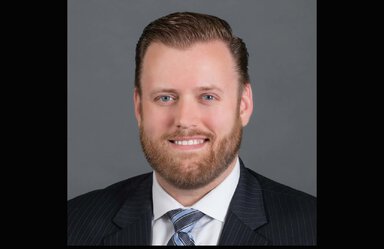 closeup of man with light brown hair and a beard. He is smiling and appears to be wearing business clothing.