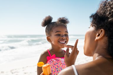 A mother boops sunscreen on her little girl's nose at the beach.