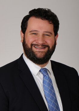 Andrew Alkis, M.D. Psychiatry Developing Teacher wearing a black suit with a blue tie
