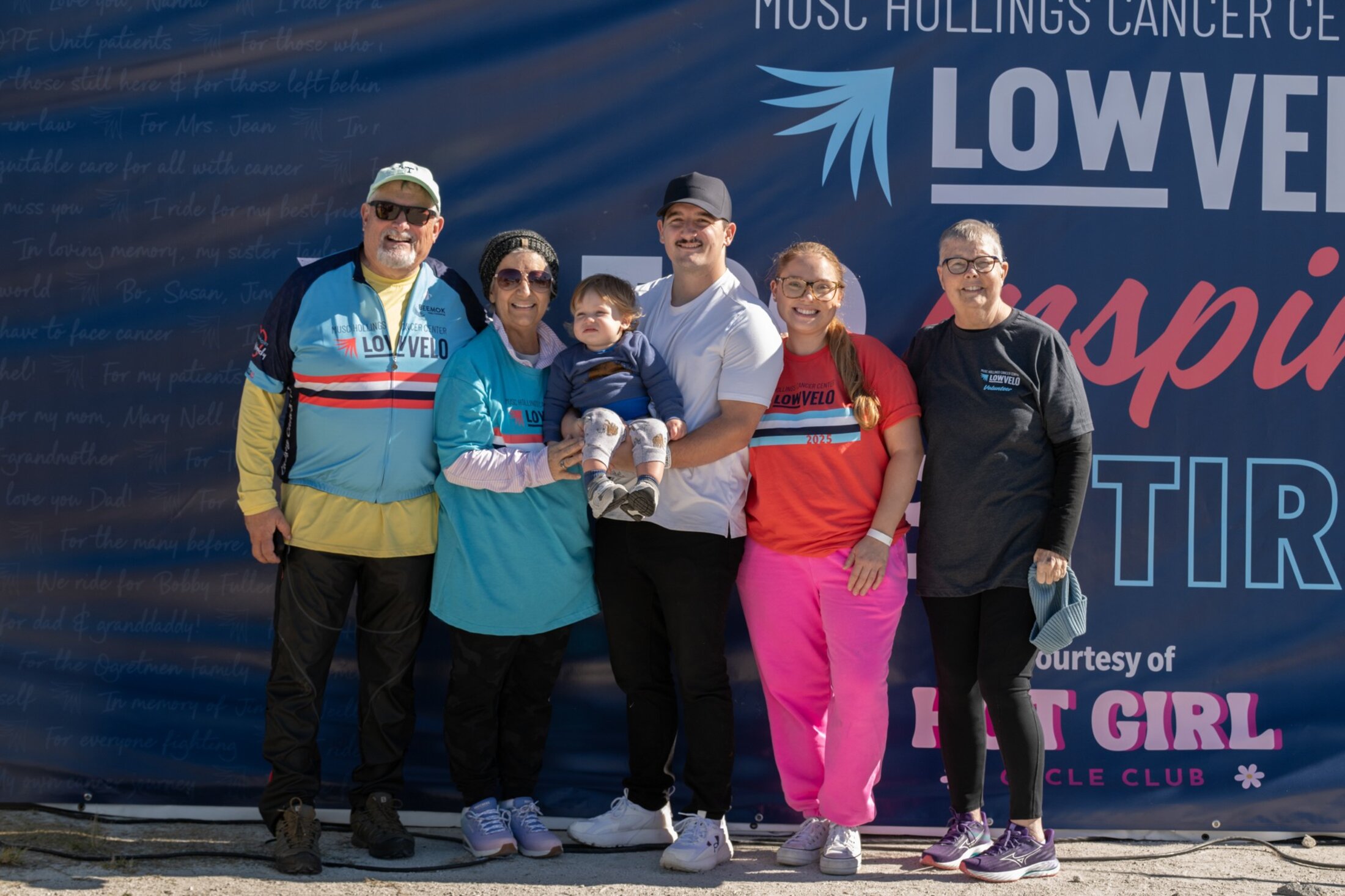 A family of five adults of various ages and a toddler pose in athletic gear in front of a LOWVELO sign at an outdoor event.
