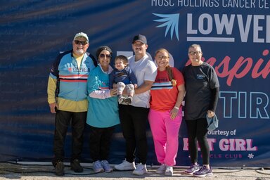 A family of five adults of various ages and a toddler pose in athletic gear in front of a LOWVELO sign at an outdoor event.