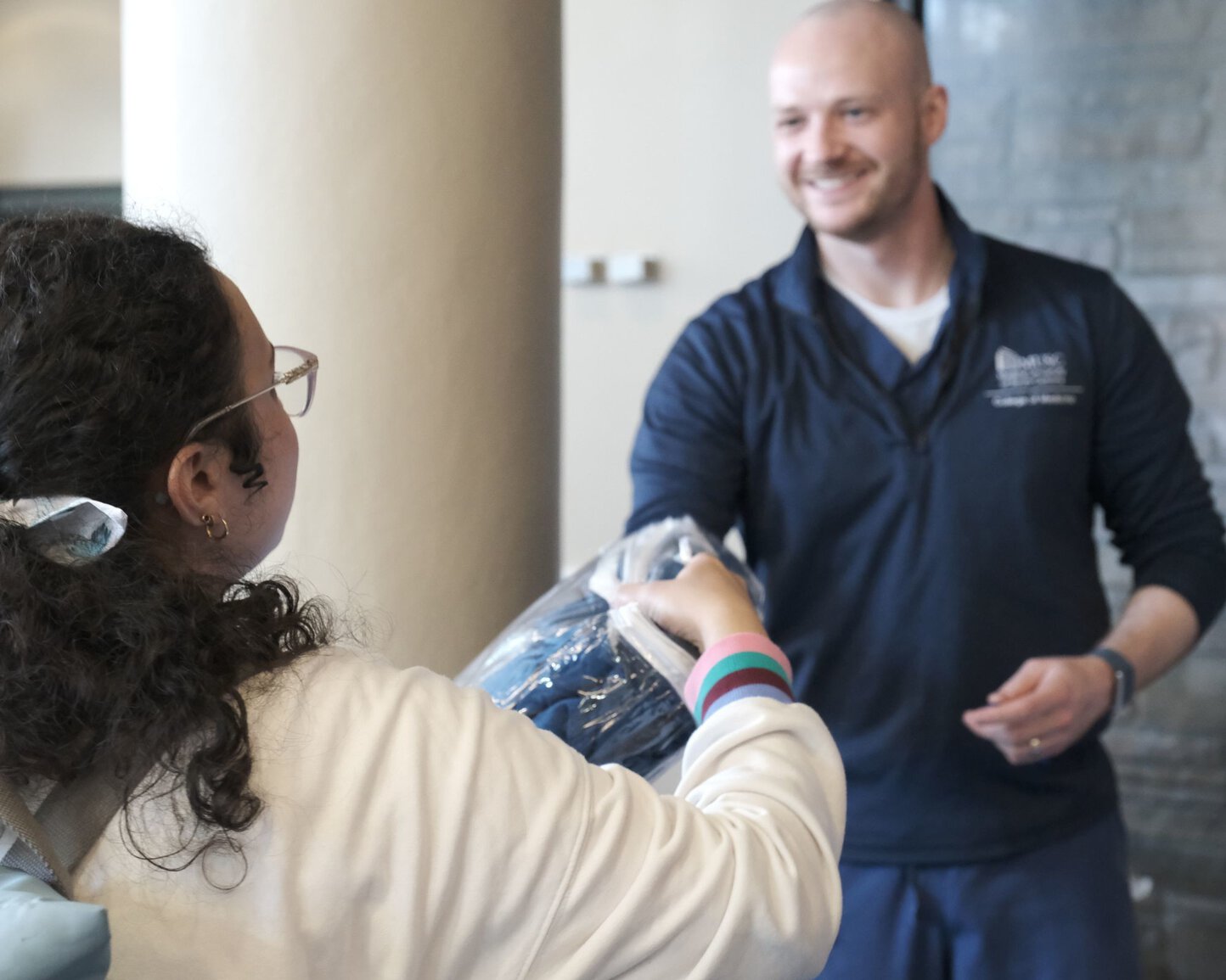 Two people exchanging an item indoors near a column.