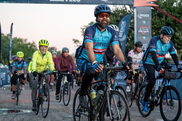 a large group of cyclists ride under the Lowvelo25 starting line truss
