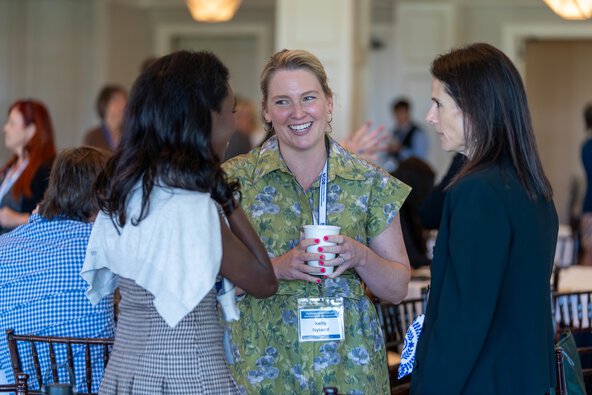 Three women stand together and talk at an event.