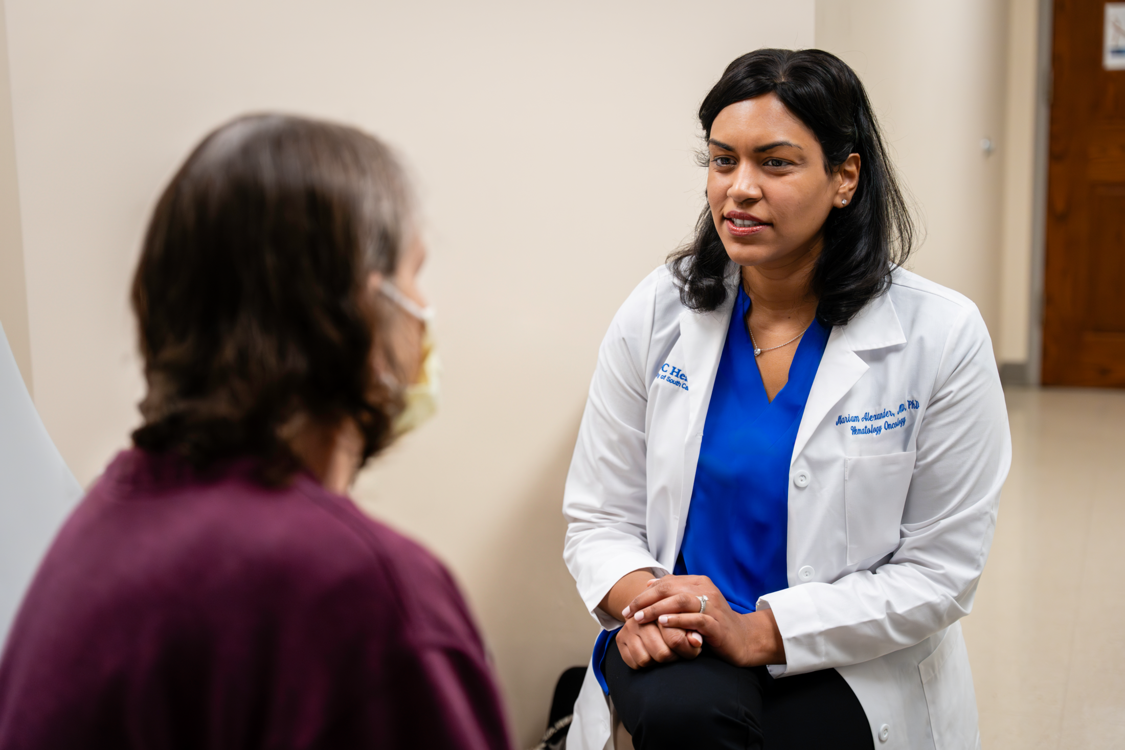 A doctor sits in an exam room and chats with a patient.
