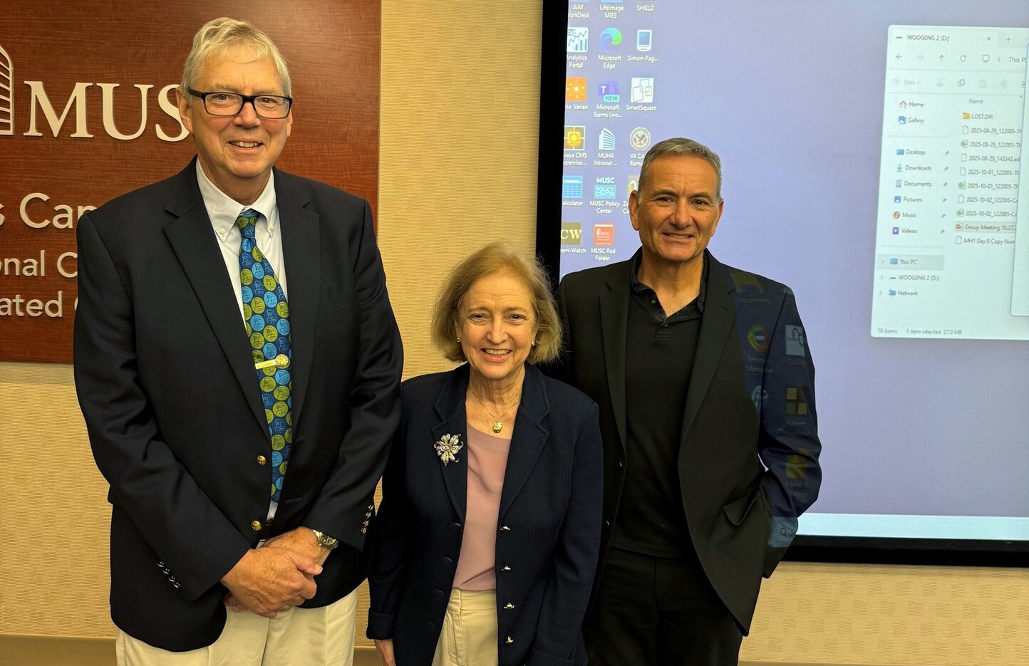 Three people stand together for a photo in a conference room.