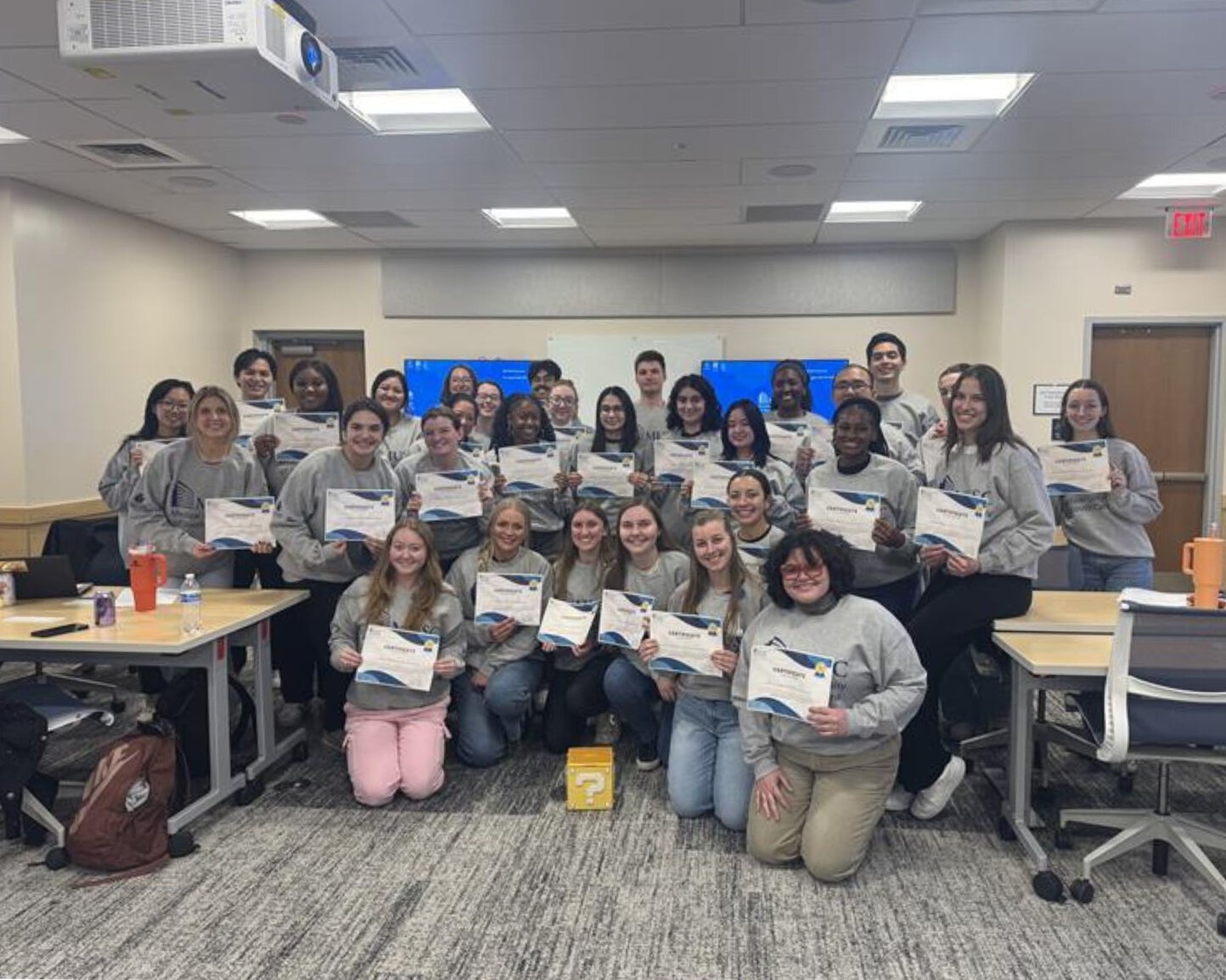Group of students in a classroom holding certificates and posing together.