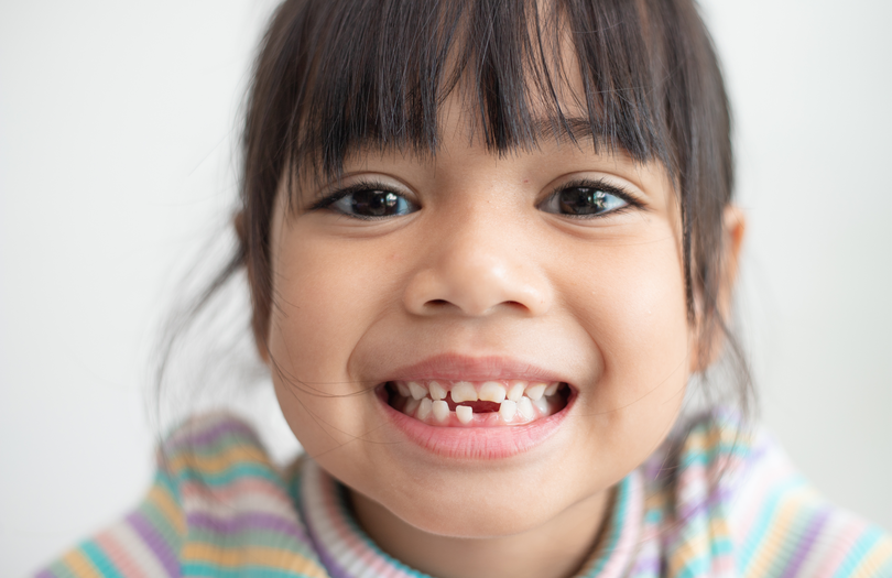 A young girls grins, showing off a missing baby tooth.